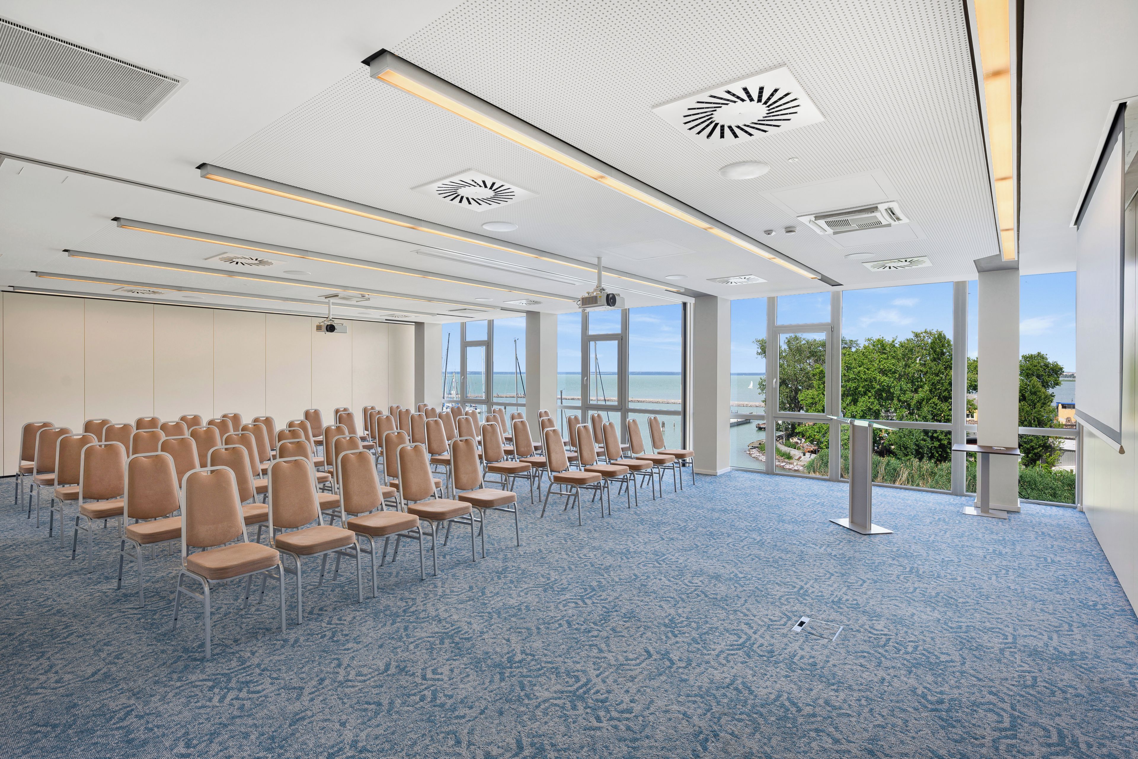 A conference room with rows of chairs, large windows, and a view of the sea.