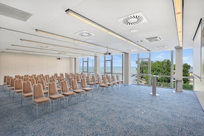 Une salle de conférence avec des rangées de chaises, de grandes fenêtres et une vue sur la mer.