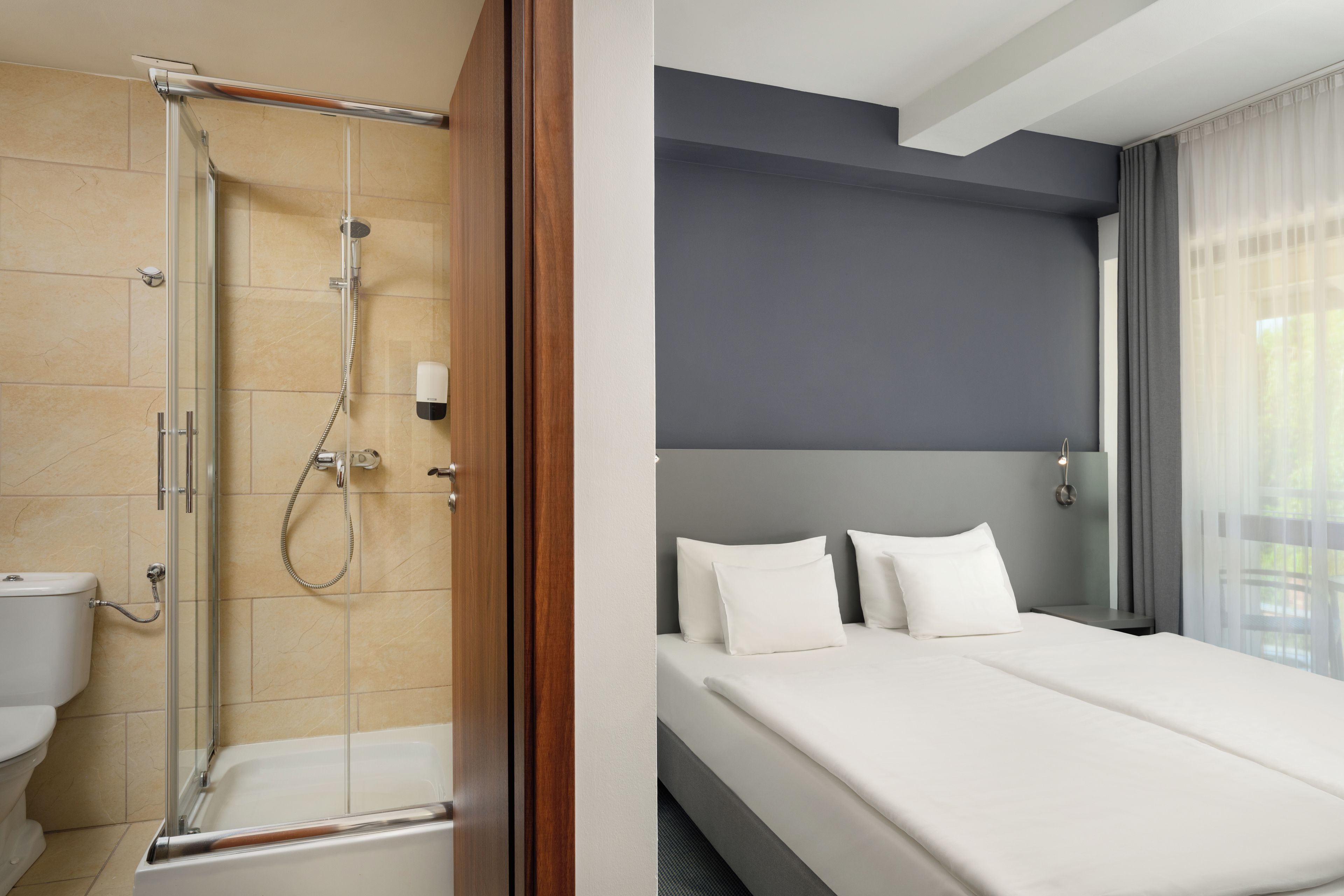 A hotel room with a shower, toilet, and a bed with white bedding.