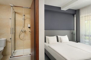 A hotel room with a shower, toilet, and a bed with white bedding.