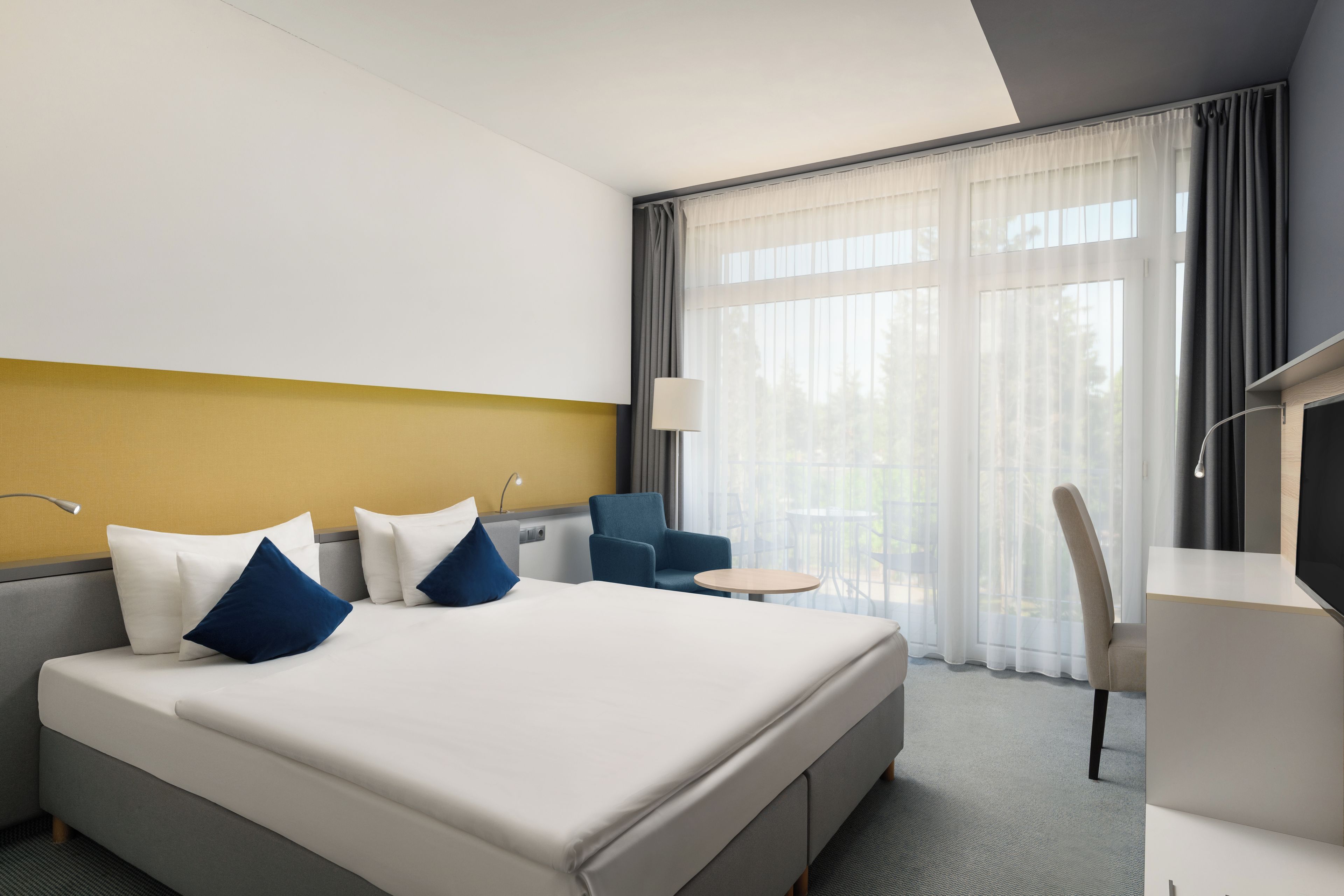 Habitación de hotel con cama, escritorio, silla y vistas al exterior.