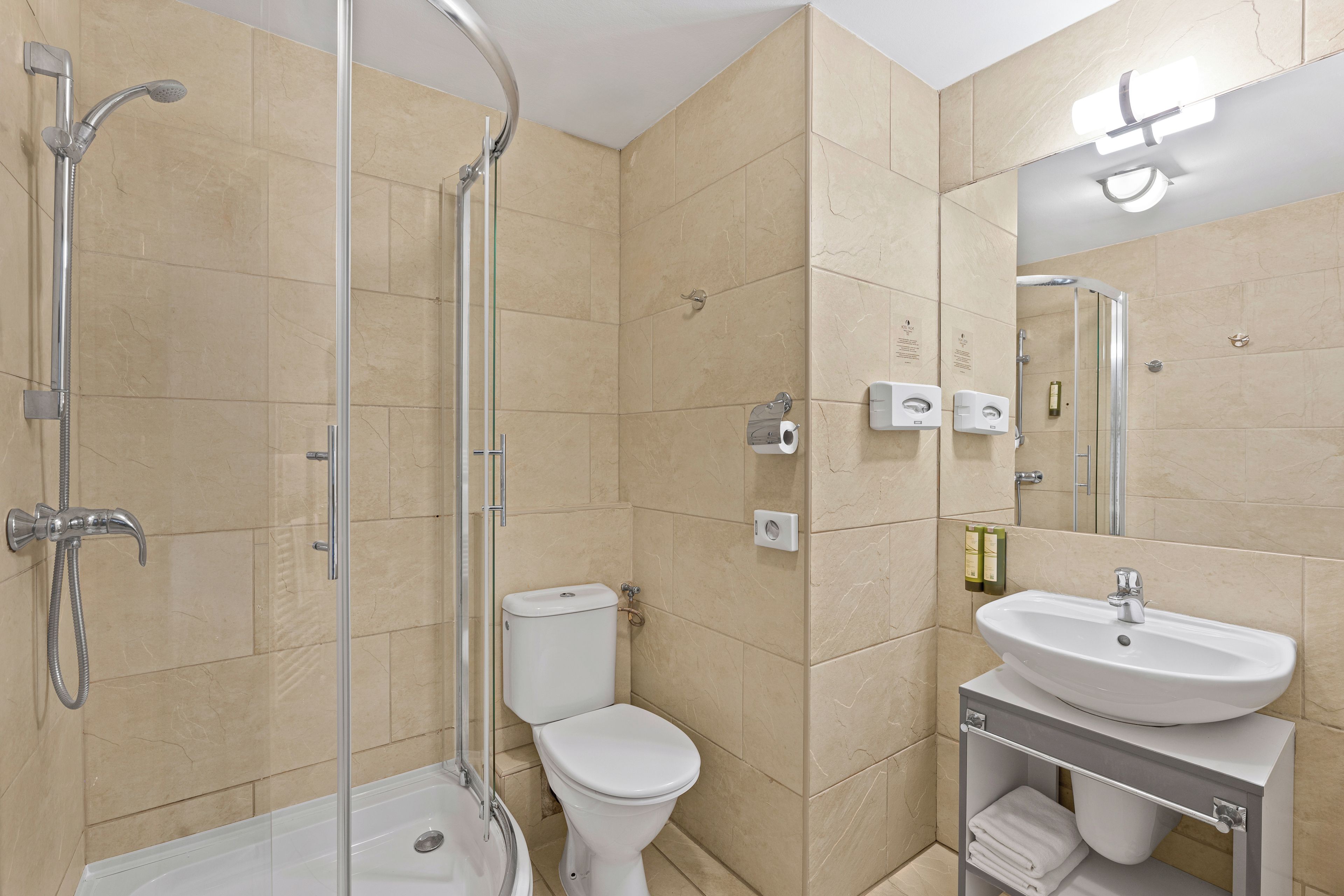 Un baño moderno con ducha de vidrio, inodoro blanco y lavamanos con toallero.
