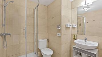 Un baño moderno con ducha de vidrio, inodoro blanco y lavamanos con toallero.