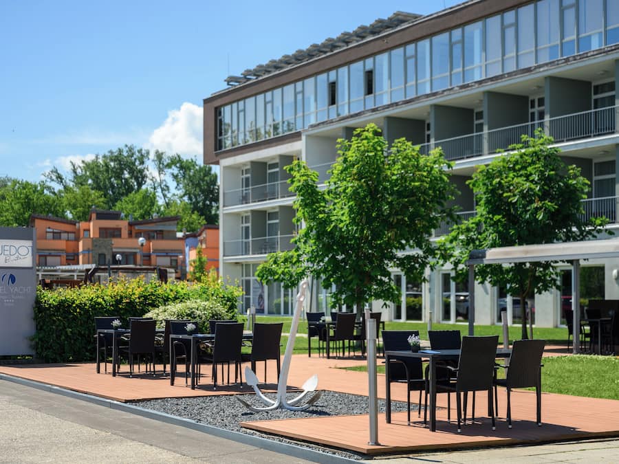 Exterior de un hotel con terraza, un cartel y un edificio de varios pisos.