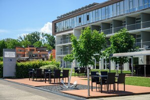 A hotel exterior with outdoor seating, a signboard, and a building with multiple floors. - Hotel Yacht Wellness & Business (Siófok)