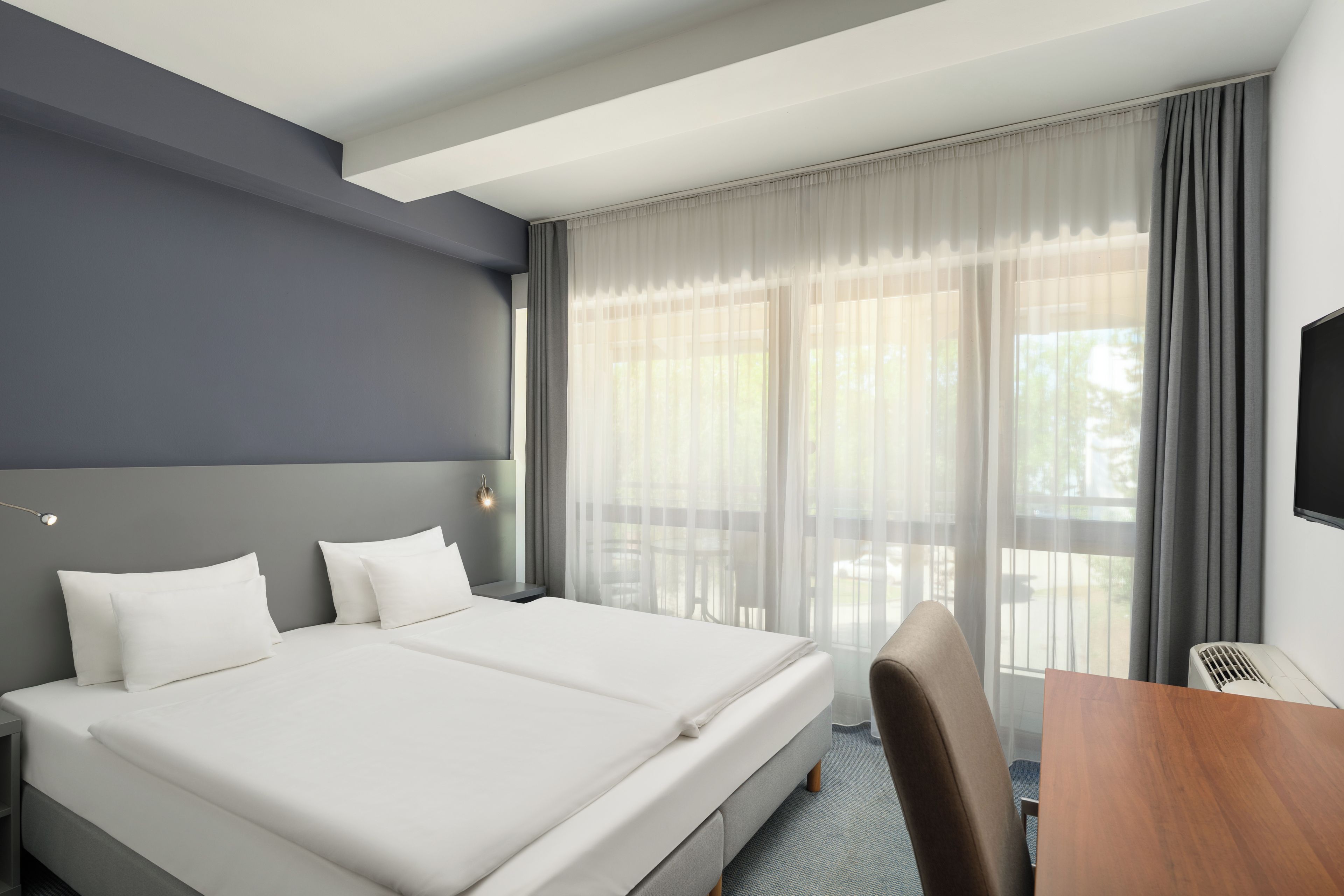 Una habitación de hotel con una cama grande, un escritorio, una silla y un televisor.