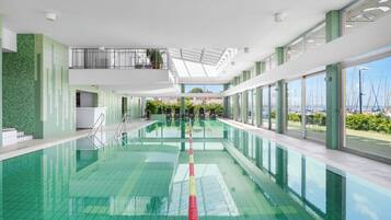 Una piscina interior moderna con agua cristalina, un bloque de salida y vistas al mar a través de amplios ventanales.