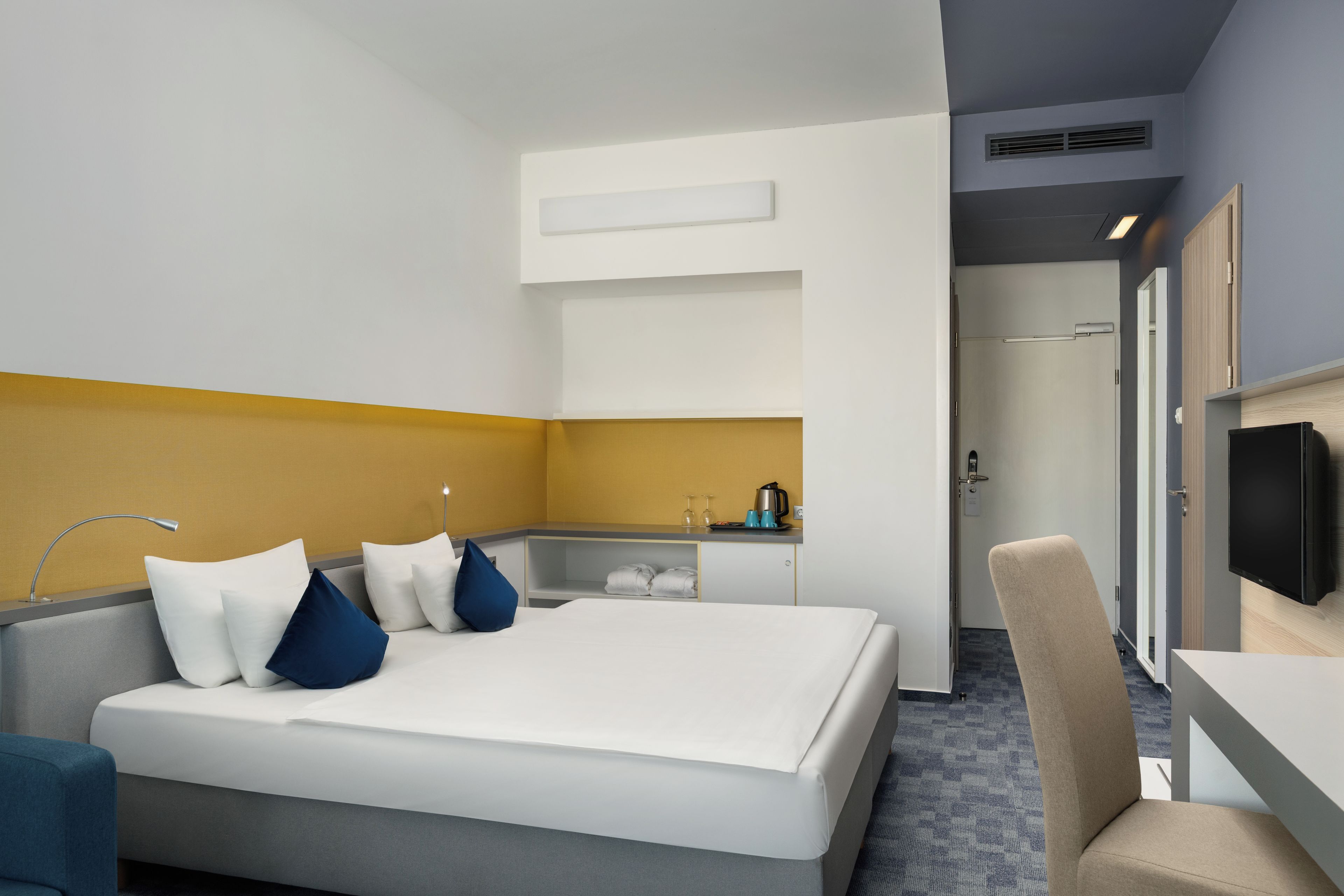 Habitación de hotel con una cama, un escritorio, una silla, un televisor y un baño visible a través de una puerta abierta.