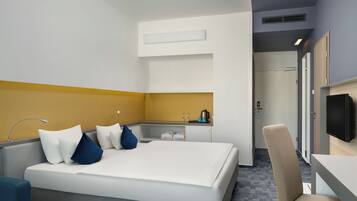 Habitación de hotel con una cama, un escritorio, una silla, un televisor y un baño visible a través de una puerta abierta.