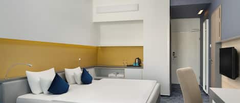A hotel room with a bed, a desk, a chair, a TV, and a bathroom visible through an open door.