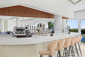 A modern bar area with a counter, stools, and a coffee machine.
