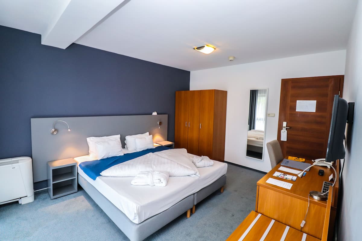 Una habitación de hotel moderna con una cama grande, mesitas de noche, un escritorio con una silla, un armario y un televisor.