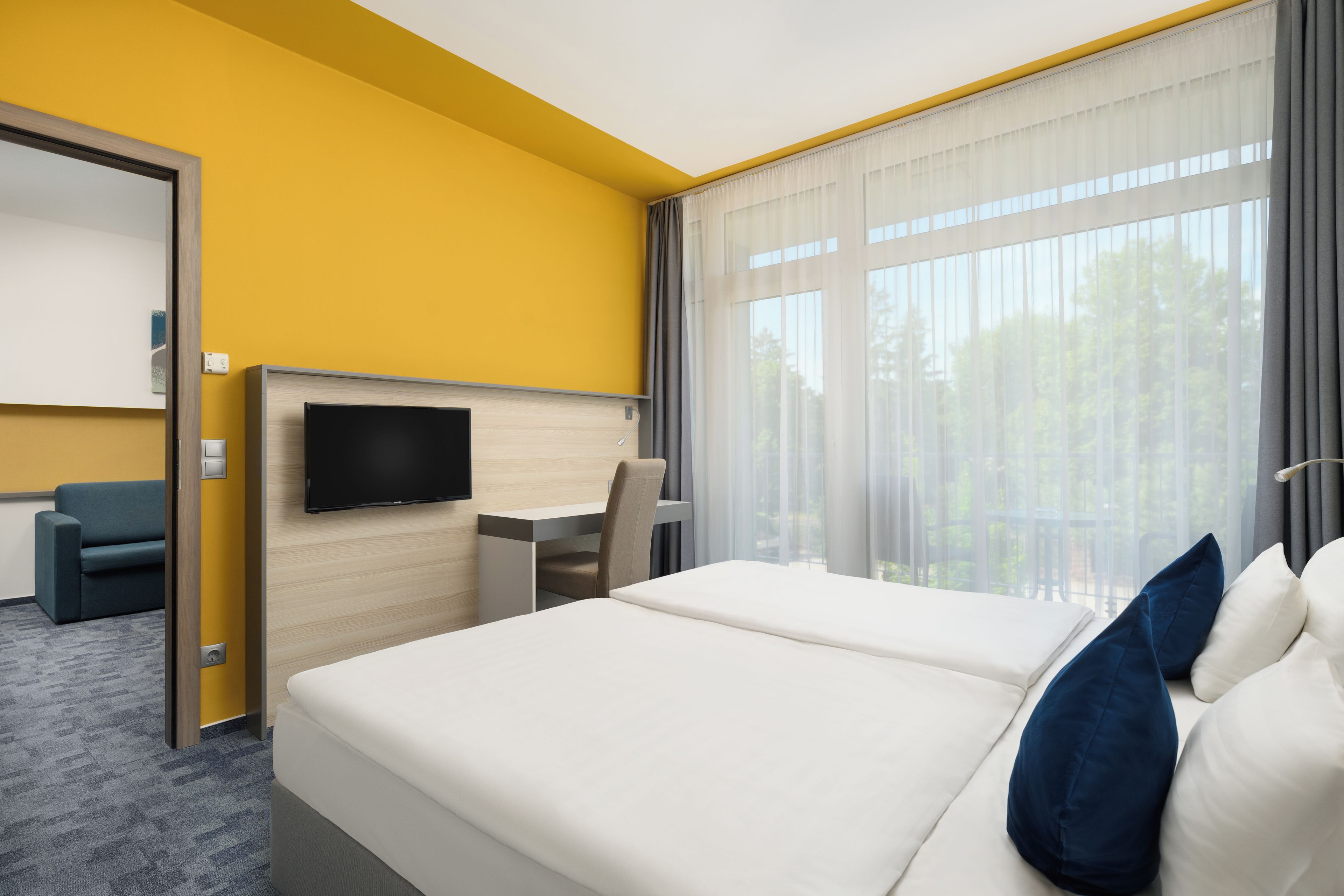 A hotel room with a bed, a desk, a chair, a television, and a large window with curtains.