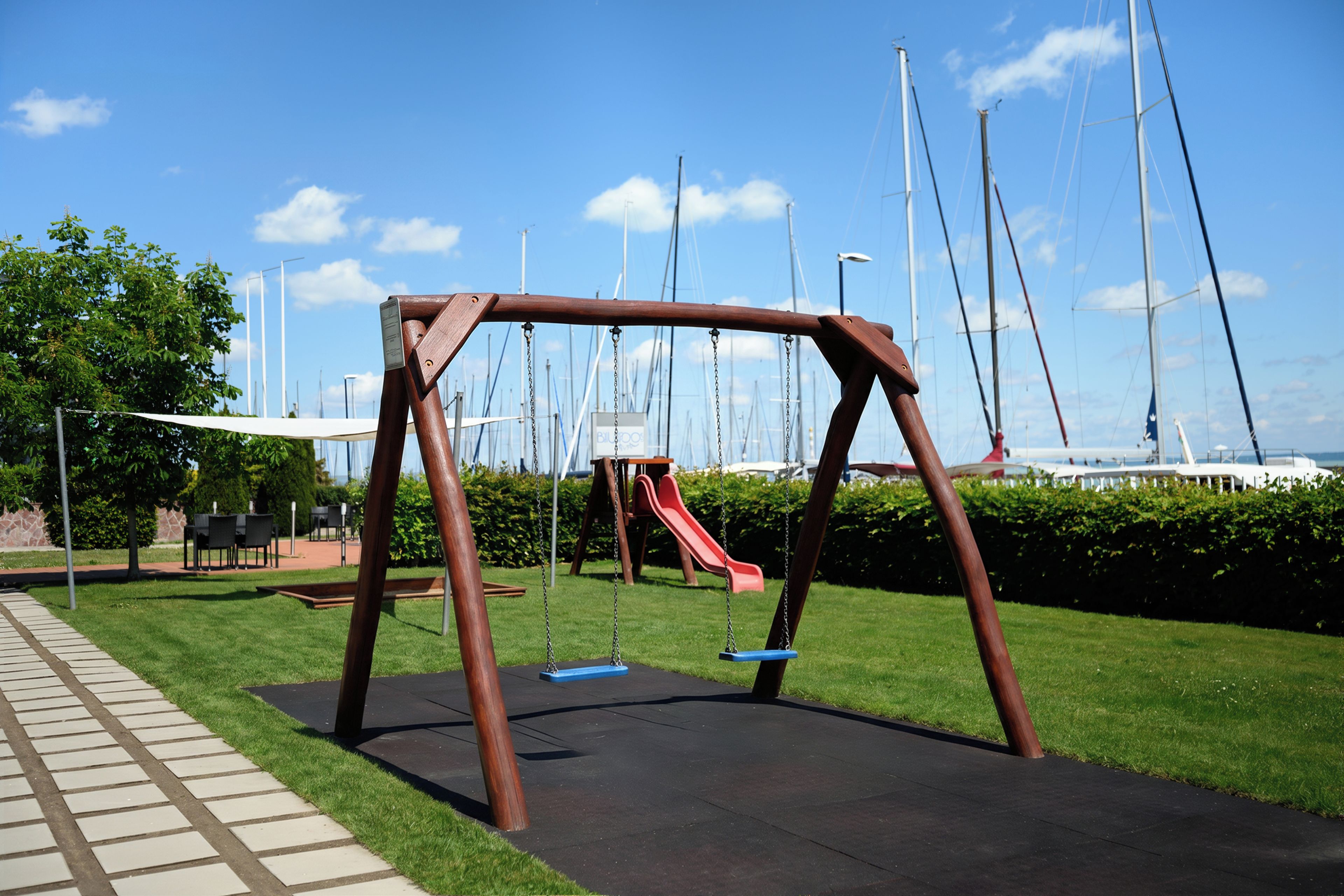 Un parque infantil con columpios y un tobogán, rodeado de césped y un sendero pavimentado.