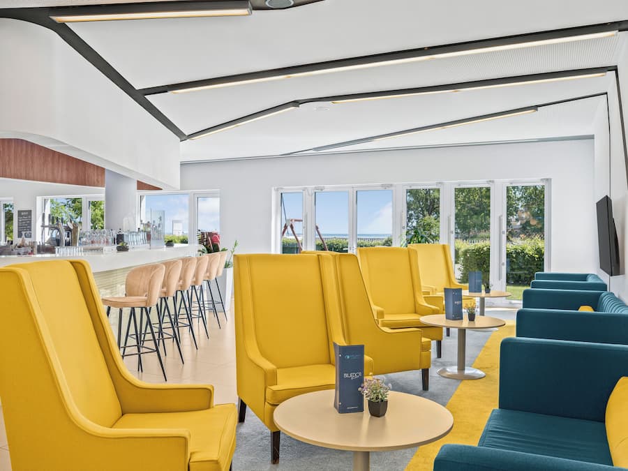 Et moderne loungeområde med gul og blå siddeplads, en bar med skrammel og store vinduer med udsigt til det fri.