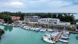 A marina with multiple boats docked, a modern building with a glass facade, and a view of the surrounding landscape.