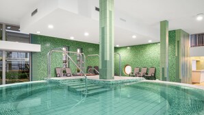 Une piscine intérieure moderne avec un mur décoré de mosaïques vertes, un escalier d’accès à la piscine et des chaises longues.