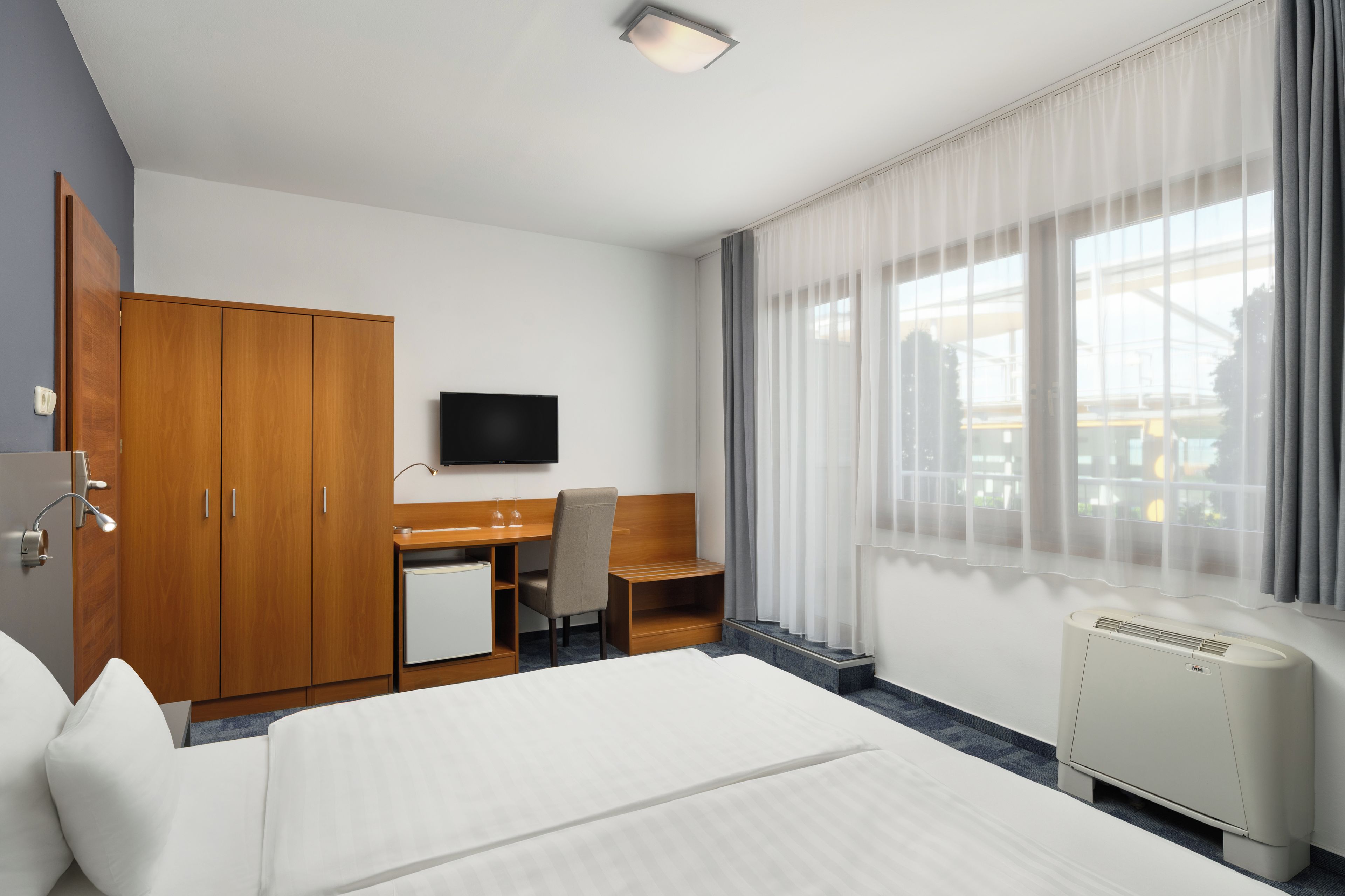 A hotel room with a bed, a desk, a chair, a television, and a window with curtains.