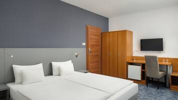 A hotel room with a bed, a desk, a chair, a television, and a wardrobe.