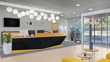 Un mostrador de recepción de hotel con diseño moderno, un televisor de pantalla plana y el logotipo de 'HOTEL YACHT Wellness & Business Söfok' en la pared.