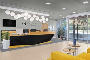 A hotel reception desk with a modern design, a flat-screen TV, and a logo for 'HOTEL YACHT Wellness & Business Söfok' on the wall.