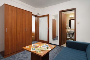 Une chambre d’hôtel avec une armoire en bois, une petite table sur laquelle est posé un jeu de société, un canapé bleu et une salle de bain visible à travers une porte ouverte.
