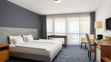 Ein Hotelzimmer mit einem großen Bett, einem Schreibtisch mit Stuhl, einem Fernseher und einem Fenster mit Vorhängen.