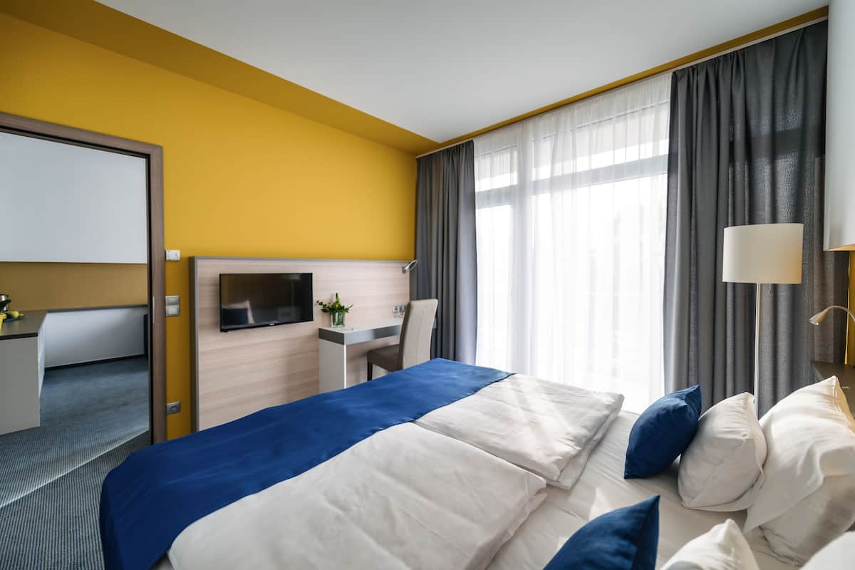 Una habitación de hotel con cama, escritorio, televisor y ventana con cortinas.
