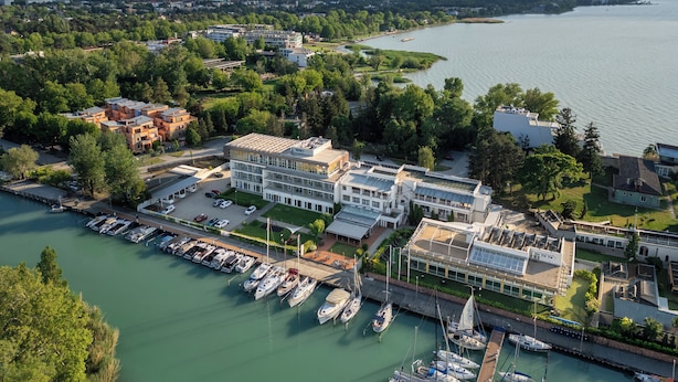 Un port de plaisance où sont amarrés de nombreux bateaux, un hôtel au design moderne et une rivière avec un pont en arrière-plan.
