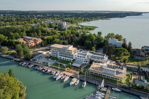 Een jachthaven met verschillende boten afgemeerd, een hotel met een modern design, en een rivier met een brug op de achtergrond.