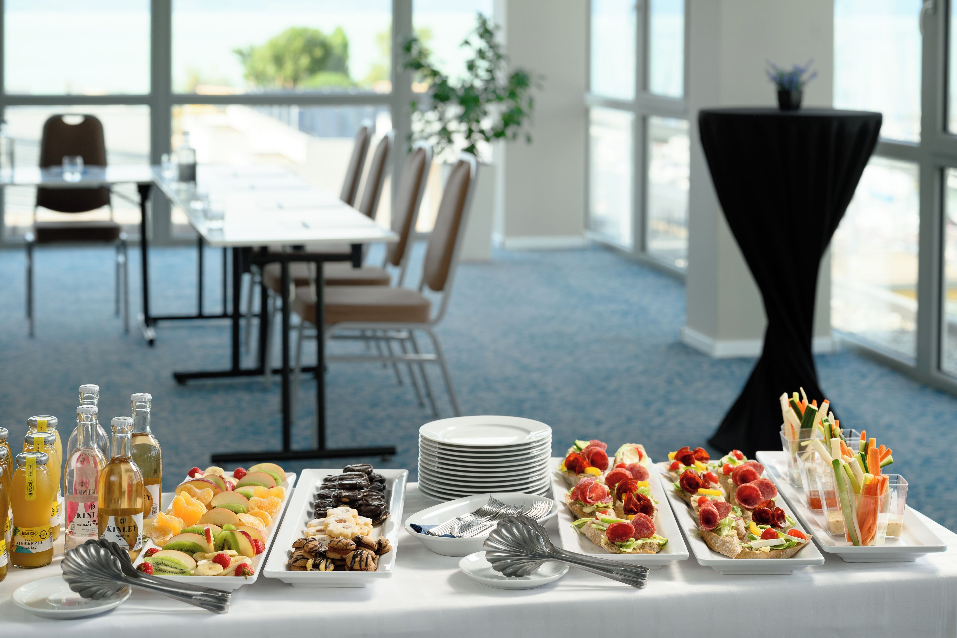 Una mesa de buffet con diversos alimentos y salsas, un comedor con sillas y una mesa, y vistas al exterior a través de amplios ventanales.