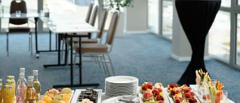 A buffet table with various food items and condiments, a dining area with chairs and a table, and a view of the outdoors through large windows.
