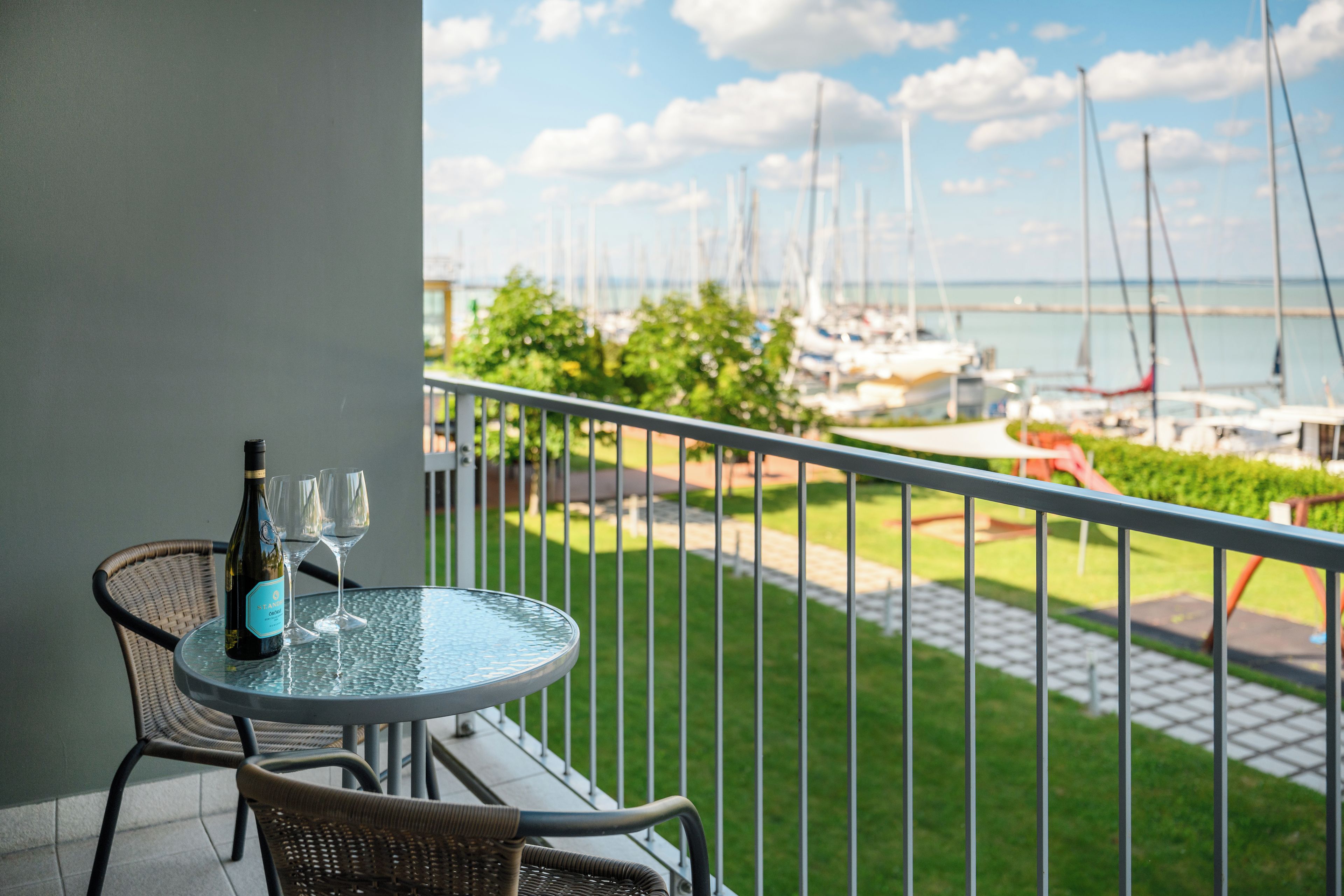 A balcony with a table and chairs, a bottle of wine, and a view of a marina with boats.