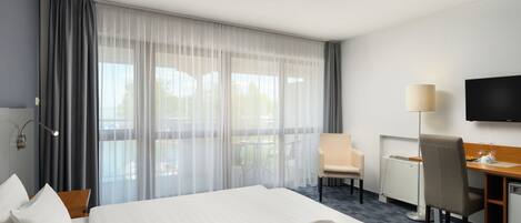A hotel room with a large bed, a desk, a chair, a television, and a view of the outdoors.