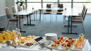 A buffet table with various food items and drinks, surrounded by tables and chairs in a spacious room.