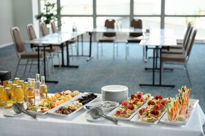 Une table de buffet garnie de divers plats et boissons, entourée de tables et de chaises dans une pièce spacieuse.