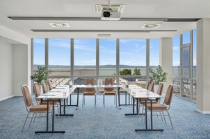 Un salón de conferencias con una gran mesa, sillas y vistas panorámicas de la ciudad a través de amplios ventanales.