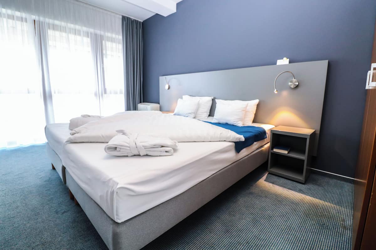 Habitación de hotel con una cama grande, una mesita de noche y una lámpara de pared.