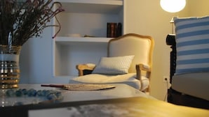 A bedroom with a bed, a bedside table with a vase and a book, a chair with a striped pillow, and a shelf with books. - Hydras Chromata (Hydra)