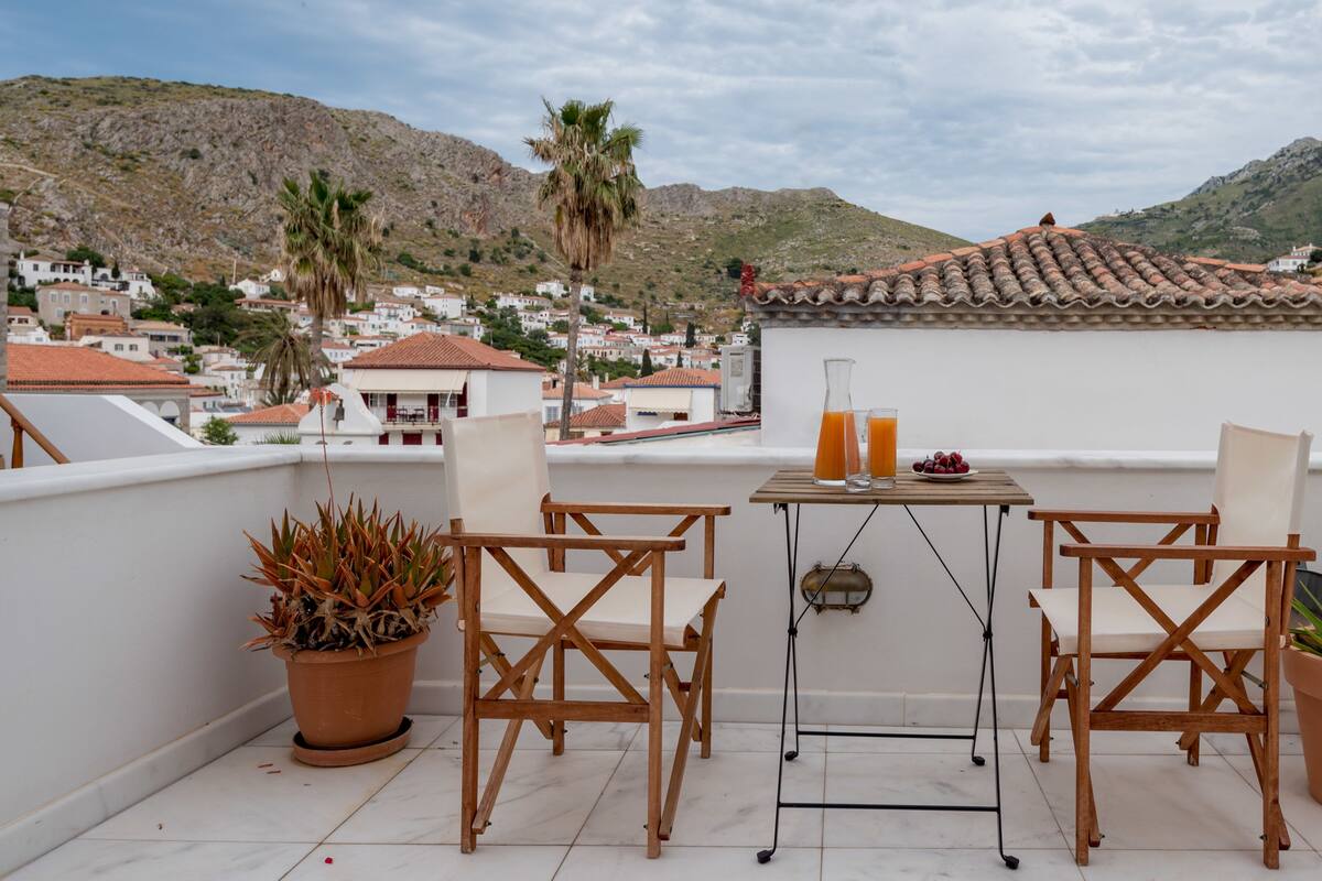 A terrace with two wooden chairs, a table with a glass of orange juice, and a potted plant.