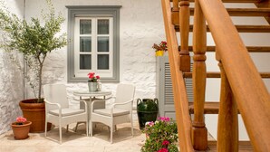 A white wicker chair and table set against a white wall with a window. - Hydras Chromata (Hydra)