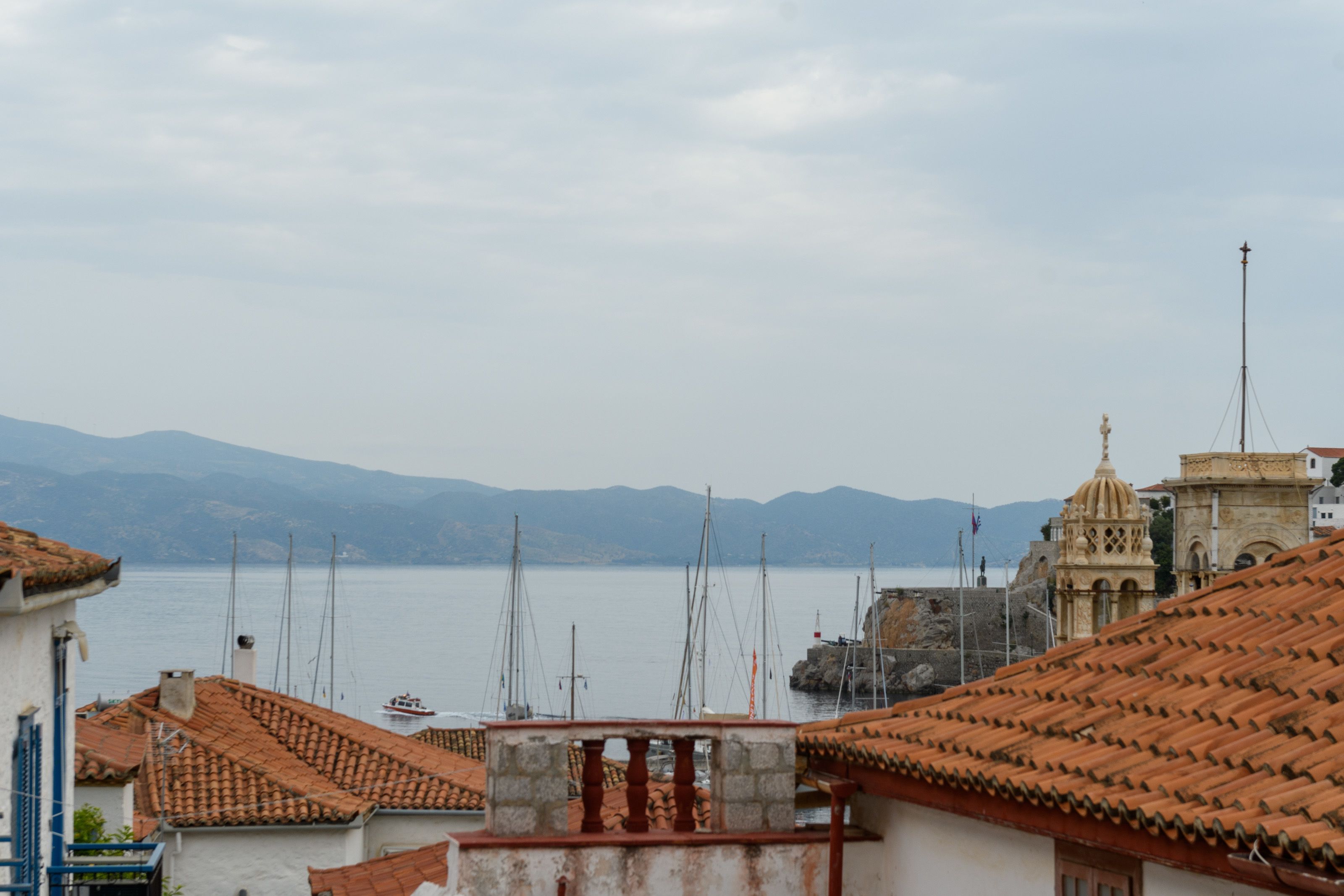 A coastal town with terracotta-roofed buildings, a prominent church with a dome, and a calm sea in the background.