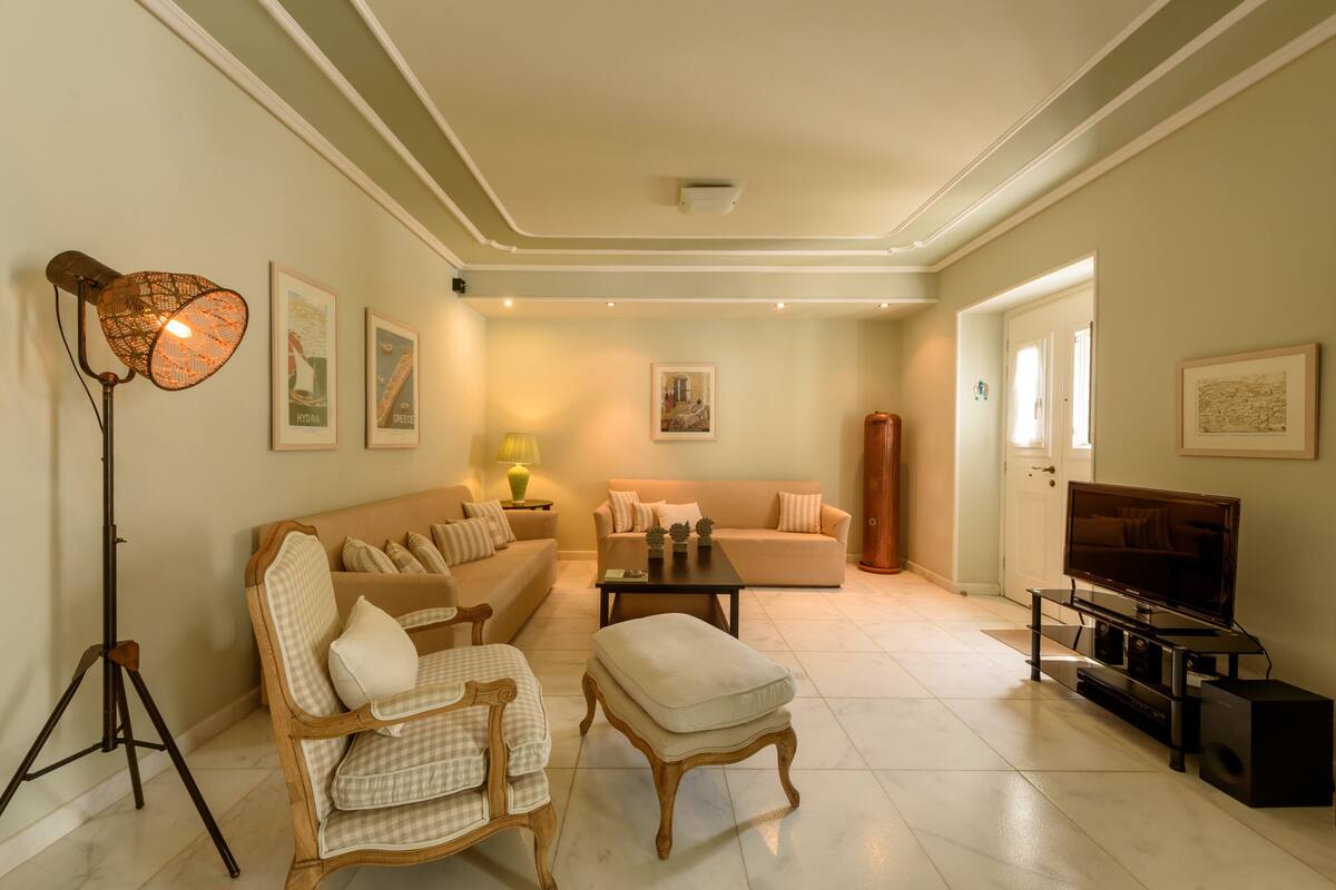 A spacious living room with a sofa, armchairs, a coffee table, and a television on a stand.