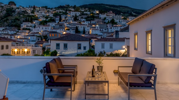 A terrace with two chairs and a table, overlooking a hillside town at dusk. - Hydras Chromata (Hydra)