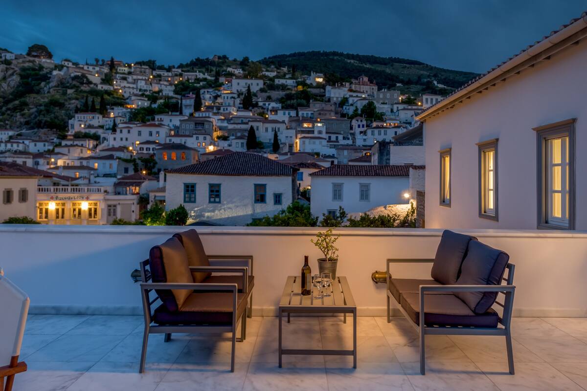 A terrace with two chairs and a table, overlooking a hillside town at dusk.