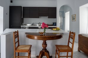 Una cocina moderna con armarios oscuros, una encimera blanca y una mesa de comedor redonda de madera con dos sillas.
