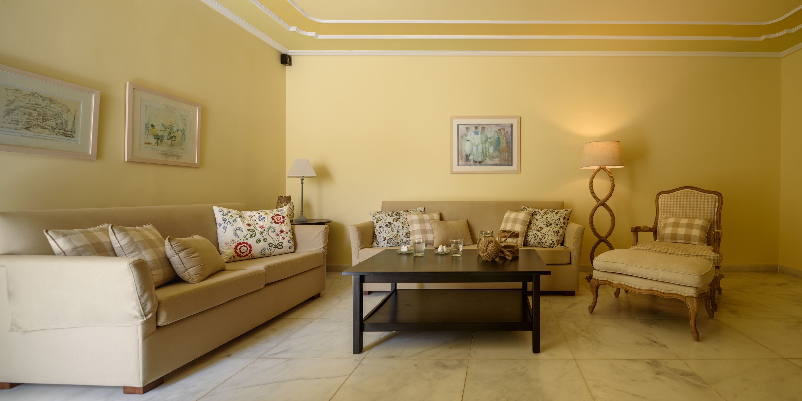 Ein Wohnzimmer mit einem beigen Sofa, einem Couchtisch, einem Sessel und gerahmten Kunstwerken an den Wänden.