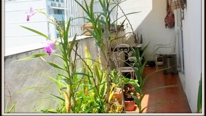 Un balcón con plantas en macetas, una silla de metal y una pared blanca con un adorno colgante.