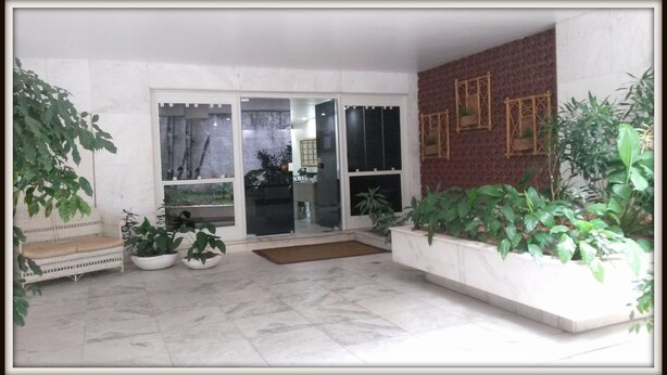 Un espacio interior amplio con suelo de baldosas, un banco, plantas en macetas y una puerta que da a otra habitación.
