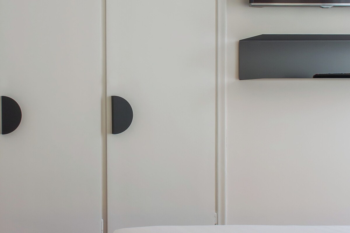 A bedroom with a bed, a TV mounted on the wall, and a wardrobe with circular handles.